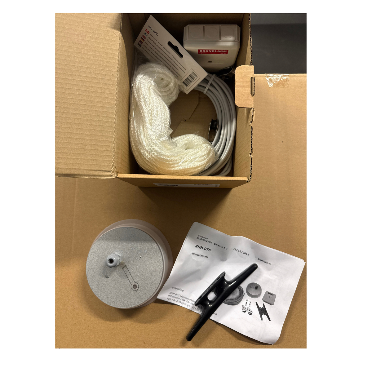 Öppen förpackning med detektorhiss RHM075 - lina, kabel, anslutningsdosa och detektorhållare med installationsanvisning
