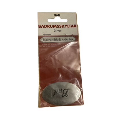 Badrumsskylt Bad i silver, oval med graverad svart text i skrivstil, i originalförpackning
